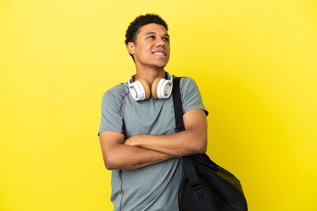 Joven deporte afroamericano con bolsa de deporte aislado sobre fondo amarillo mirando hacia arriba mientras sonríe