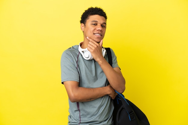 Joven deporte afroamericano con bolsa de deporte aislado sobre fondo amarillo sonriendo