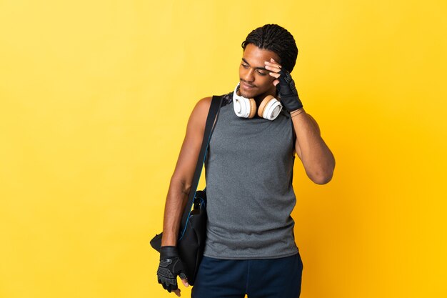 Joven deporte afroamericano con trenzas con bolsa aislado en pared amarilla riendo