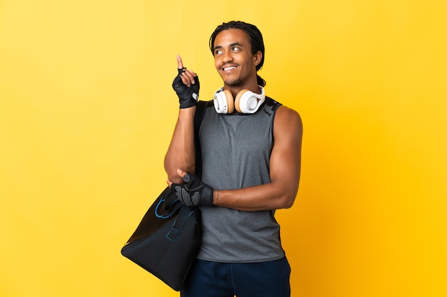 Joven deporte afroamericano con trenzas con bolsa aislado sobre fondo amarillo apuntando hacia una gran idea