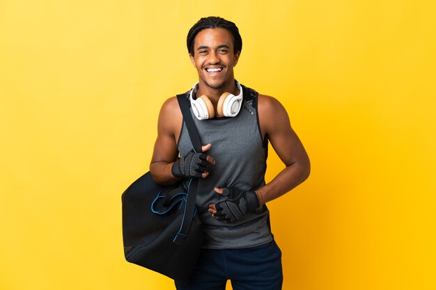 Joven deporte afroamericano con trenzas con bolsa aislado sobre fondo amarillo sonriendo mucho