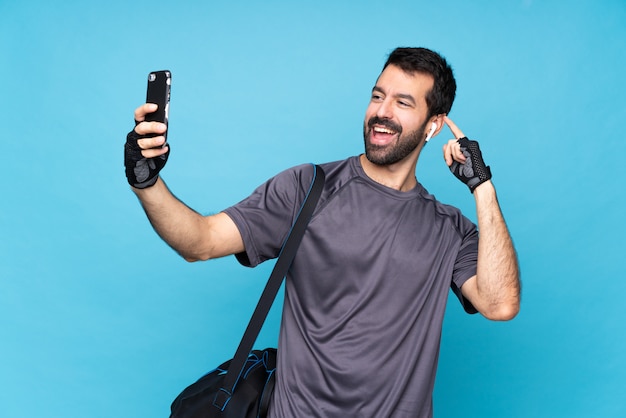 Joven deporte con barba sobre azul aislado haciendo un selfie