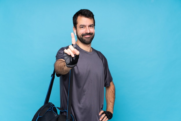 Joven deporte con barba sobre azul aislado mostrando y levantando un dedo