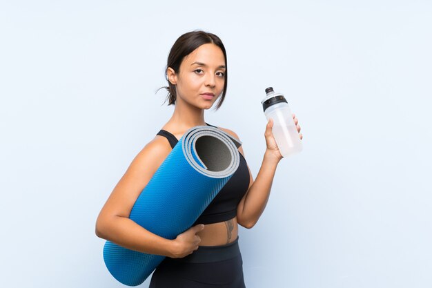 Joven deporte chica con colchoneta y con una botella de agua sobre azul aislado