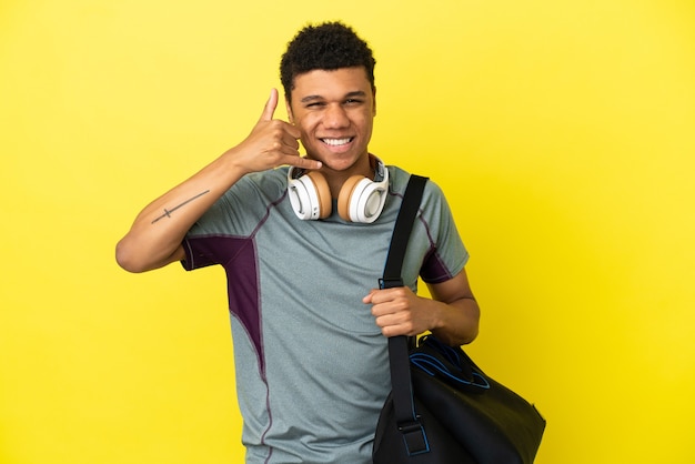 Joven deporte hombre afroamericano con bolsa de deporte aislado sobre fondo amarillo haciendo gesto de teléfono. Llámame señal