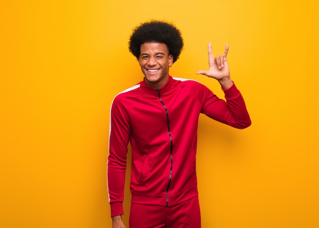 Joven deporte hombre negro sobre una pared naranja haciendo un gesto de rock