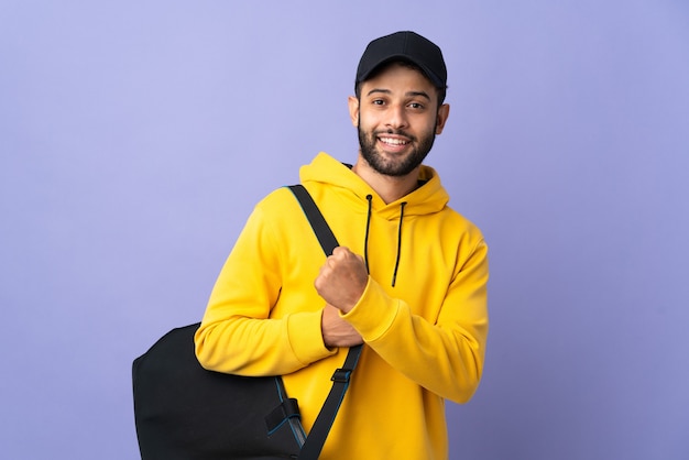 Joven deporte marroquí con bolsa de deporte aislado en púrpura celebrando una victoria