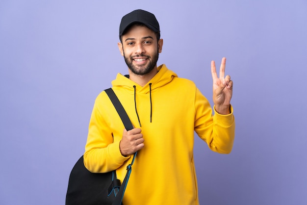 Joven deporte marroquí con bolsa de deporte en púrpura sonriendo y mostrando el signo de la victoria