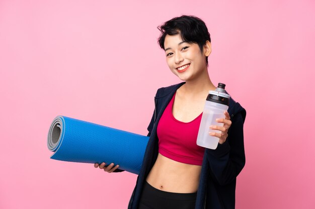 Joven deporte mujer asiática sobre pared rosa aislado con botella de agua deportiva y con una estera