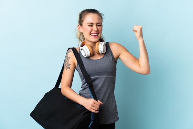 Joven deporte mujer brasileña con bolsa de deporte aislado en azul haciendo un gesto fuerte