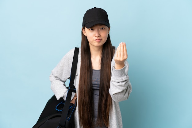 Foto joven deporte mujer china con bolsa de deporte sobre pared azul aislada haciendo gesto italiano