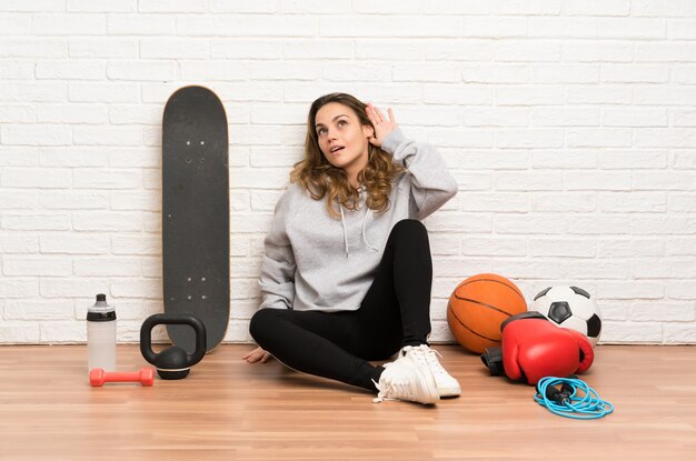 Joven deporte mujer sentada en el suelo escuchando algo