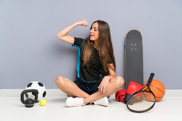 Joven deporte mujer sentada en el suelo haciendo un gesto fuerte