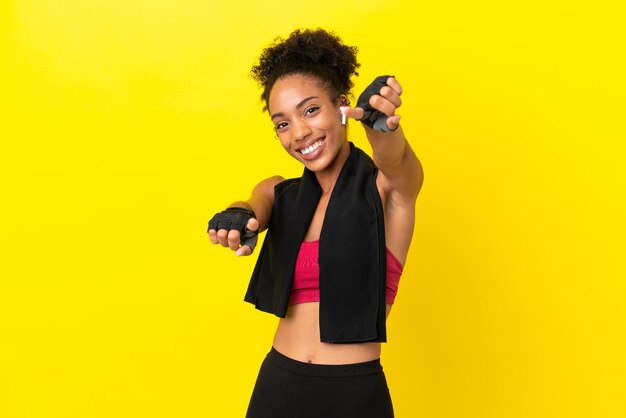 Una joven deportista africana aislada de fondo amarillo te señala con el dedo mientras sonríe