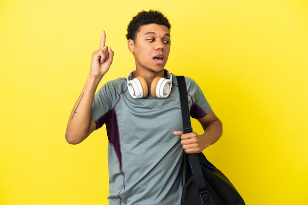 Joven deportista afroamericano con bolsa de deporte aislado sobre fondo amarillo con la intención de darse cuenta de la solución mientras levanta un dedo hacia arriba