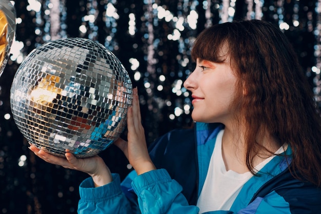 Joven deportista de los años 80 y 90 estilo chica positiva de la moda de los 90 en la fiesta disco con bola de discoteca en las manos