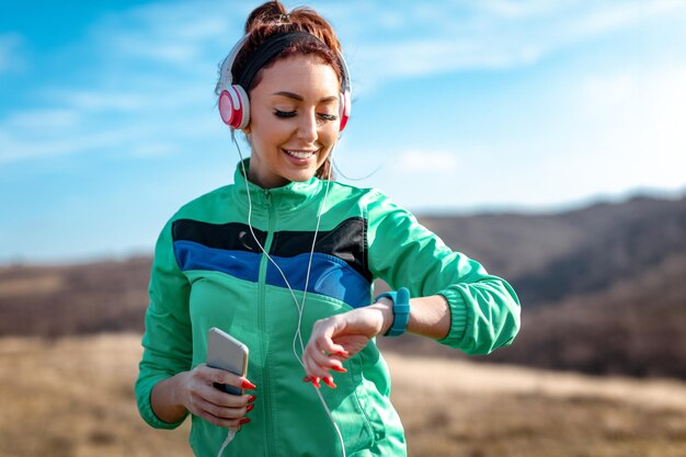 Joven deportista con auriculares mirando un cronómetro antes de entrenar en la naturaleza.