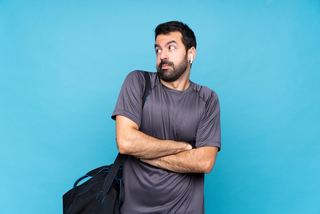 Joven deportista con barba sobre azul haciendo dudas gesto mientras levanta los hombros