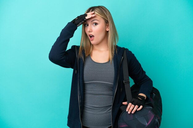 Joven deportista con bolsa deportiva aislada de fondo azul haciendo un gesto sorpresa mientras mira hacia un lado