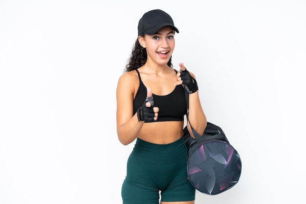 Joven deportista con bolsa deportiva aislada de fondo blanco apuntando al frente y sonriendo