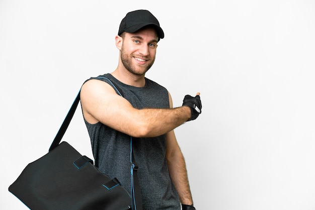 Joven deportista con bolsa deportiva sobre fondo blanco aislado apuntando hacia atrás