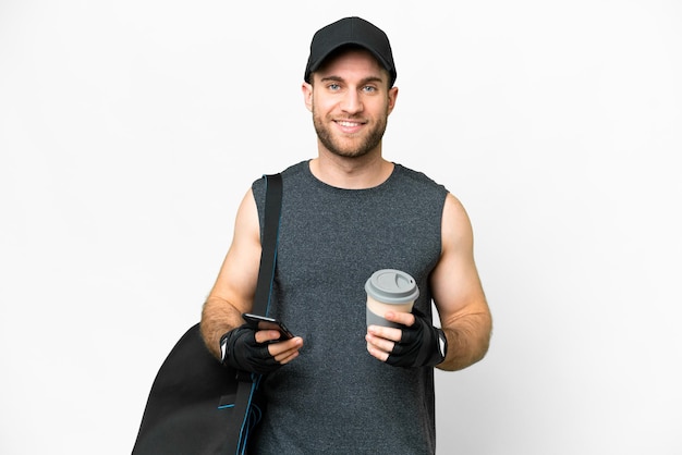 Joven deportista con bolsa deportiva sobre fondo blanco aislado sosteniendo café para llevar y un móvil