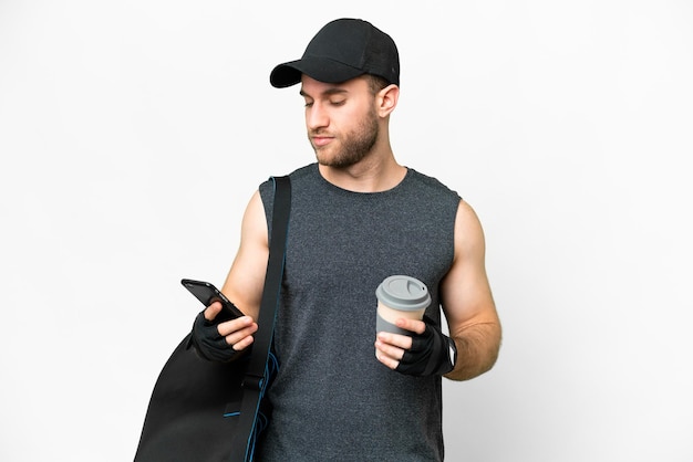 Joven deportista con bolsa deportiva sobre fondo blanco aislado sosteniendo café para llevar y un móvil