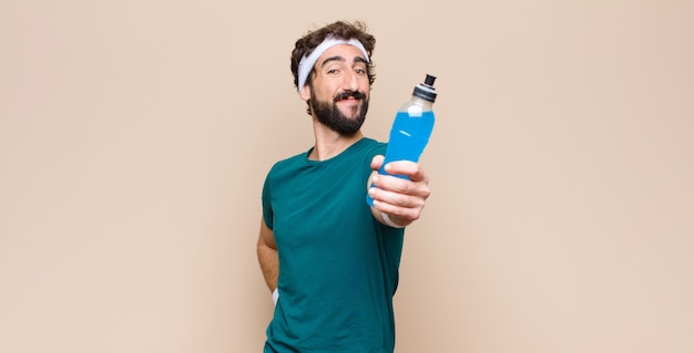 Foto joven deportista con una botella de bebida energética contra la pared plana