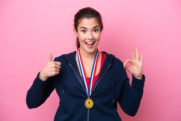 Joven deportista brasileña con medallas aisladas en un fondo rosado que muestra el signo de ok y el gesto con el pulgar hacia arriba