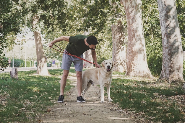 Joven deportista caminando con su perro labrador canadiense a través de un parque urbano en un día soleado