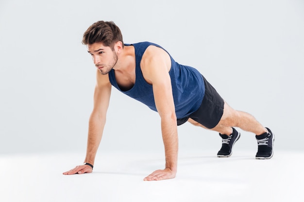 Joven deportista concentrado haciendo ejercicio y haciendo flexiones sobre fondo blanco.