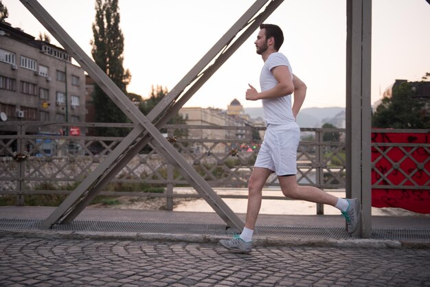 joven deportista corriendo por el puente en la mañana soleada en la ciudad