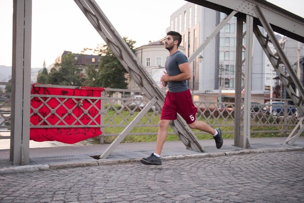 joven deportista corriendo por el puente en la mañana soleada en la ciudad