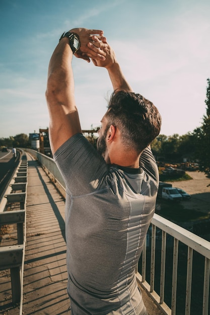 Joven deportista estirando después del entrenamiento en el puente. Vista trasera.