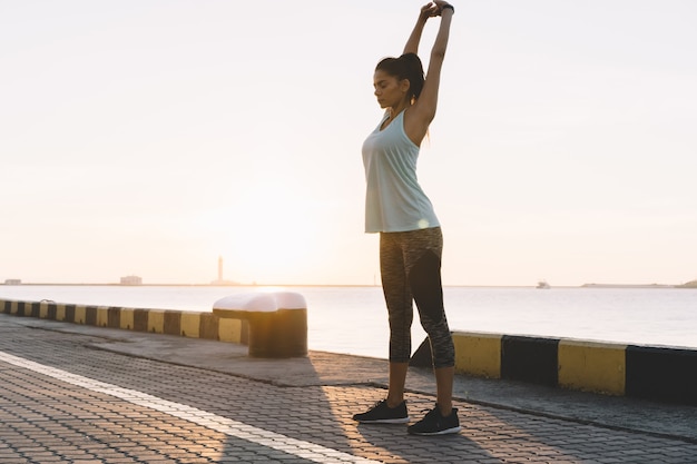 Foto joven deportista estirando y preparándose para correr cerca del puerto marítimo.