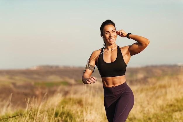 Joven deportista feliz ajustando sus auriculares mientras corre en la naturaleza Copiar espacio