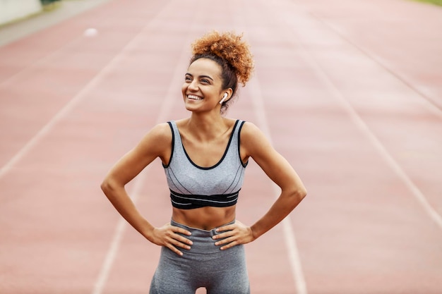 Foto una joven deportista feliz parada en el estadio con las manos en las caderas