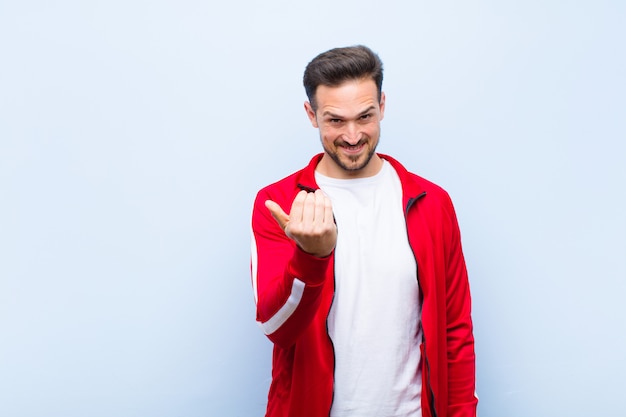 Joven deportista guapo o monitor sintiéndose feliz, exitoso y seguro, enfrentando un desafío y diciendo ¡adelante! o darle la bienvenida contra la pared plana