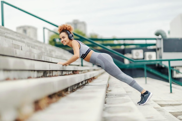 Joven deportista con hábitos saludables escucha la radio mientras hace flexiones en las escaleras en un distrito urbano