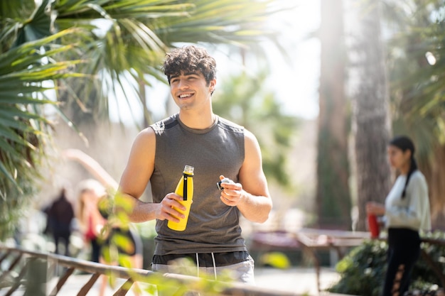 Joven deportista hace un descanso para beber agua en el parque Tiene una botella amarilla con agua