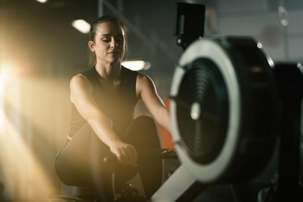 Joven deportista haciendo ejercicio en máquina de remo durante el entrenamiento deportivo en un gimnasio