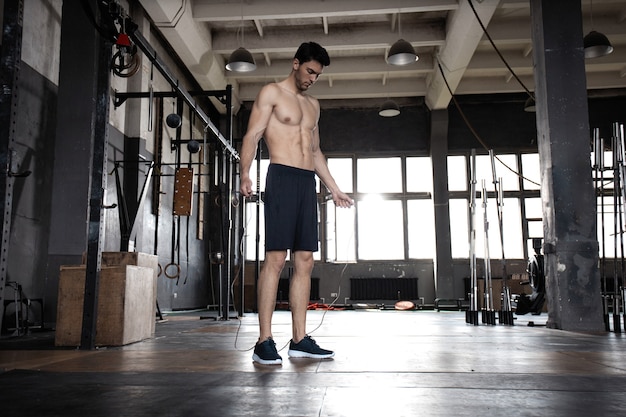 Joven deportista haciendo ejercicios de saltar la cuerda en el gimnasio.