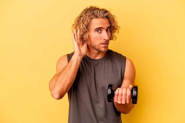 joven deportista haciendo levantamiento de pesas aislado de fondo amarillo tratando de escuchar un chisme.