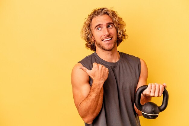 joven deportista haciendo levantamiento de pesas aislado en puntos de fondo amarillos con el dedo pulgar lejos, riendo y despreocupado.