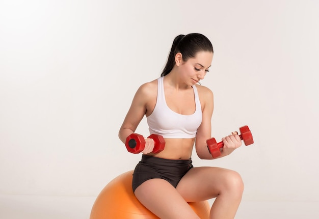 Joven deportista hermosa con pesas haciendo ejercicio en fitball