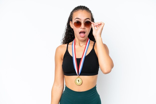 Joven deportista con medallas aisladas en fondo blanco con gafas y sorprendida