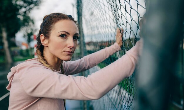 Foto joven deportista con mirada desafiante descansando en la cerca de la cancha de deportes