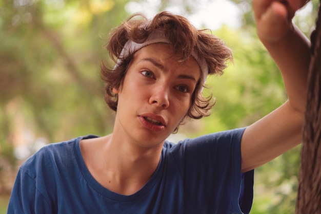 Un joven deportista mojado y cansado se apoya en el árbol después de correr por la mañana