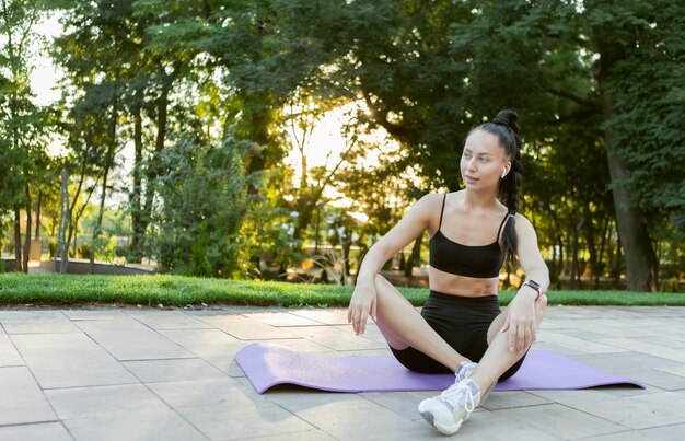 Joven deportista morena se sienta en una estera al amanecer en el parque