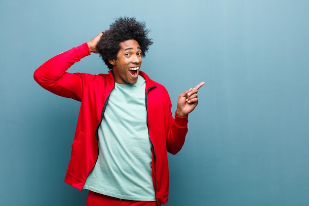 Joven deportista negro riendo, mirando feliz, positivo y sorprendido, dándose cuenta de una gran idea apuntando al espacio de copia lateral contra la pared del grunge